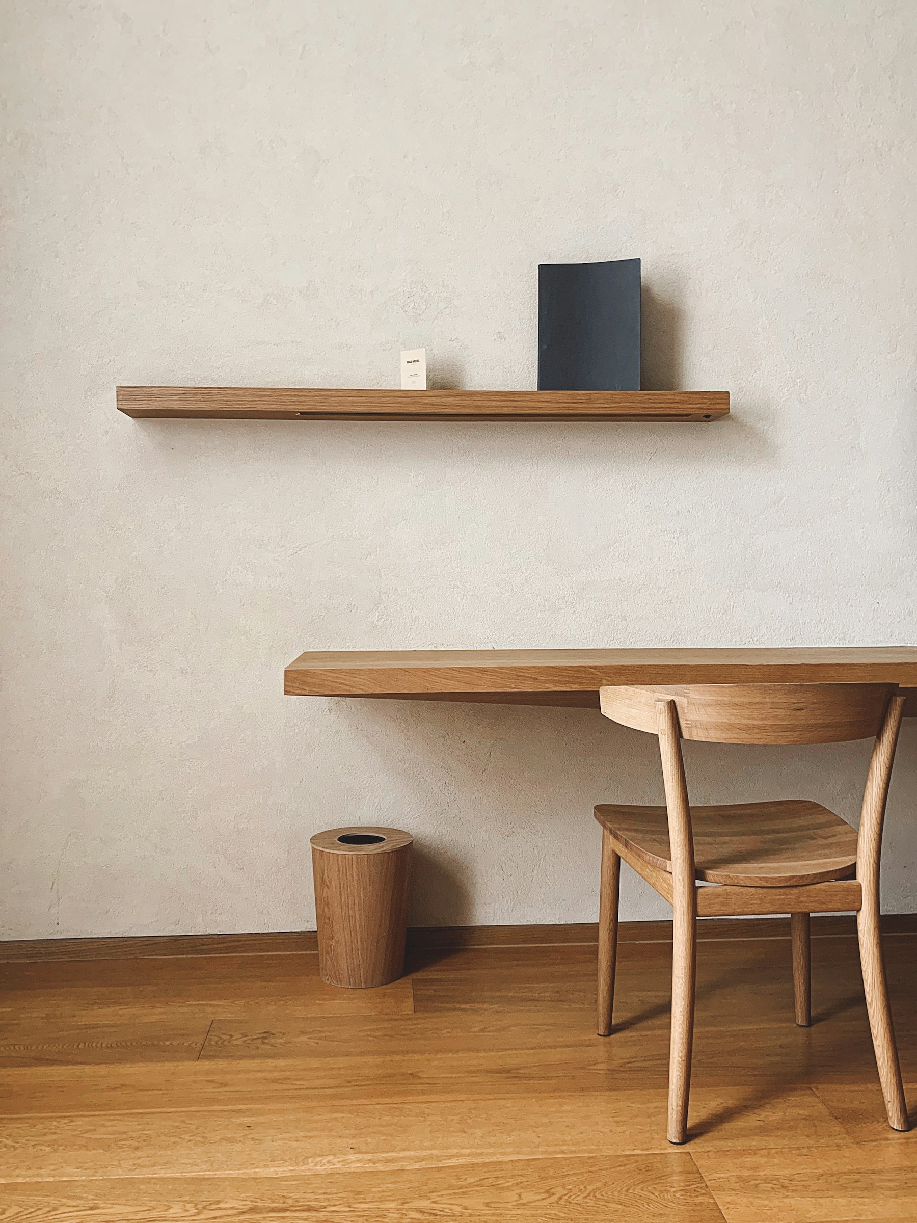 A dining table and chairs in a quiet room with a wall-mounted oak shelf